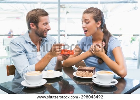 Young happy couple eating cake and man giving her a ring in the cafe
