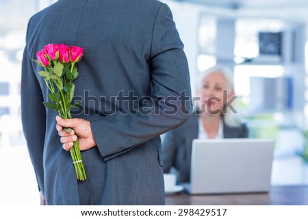 Businessman hiding flowers behind back for colleague in office