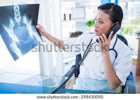 Doctor looking X-rays while having phone call in medical office