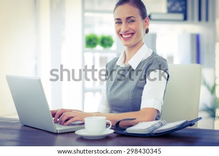 Happy businesswoman working on laptop computer and looking at camera in office