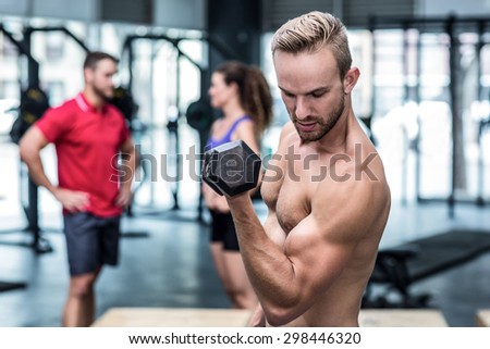 Muscular man lifting a dumbbell while looking at his biceps