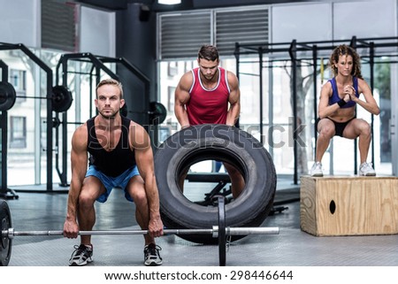 Serious three muscular people lifting and jumping in crossfit gym