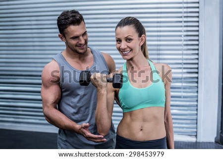 Portrait of a muscular woman lifting dumbbells helped by a coach