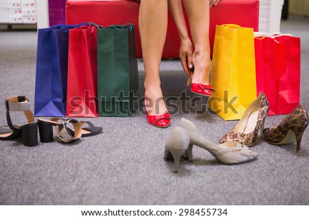 Woman sitting next to shopping bags and putting on shoes at a shoe shop