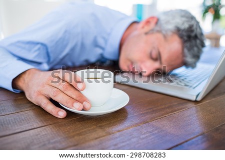 Businessman sleeping on laptop computer and touching coffee cup in office