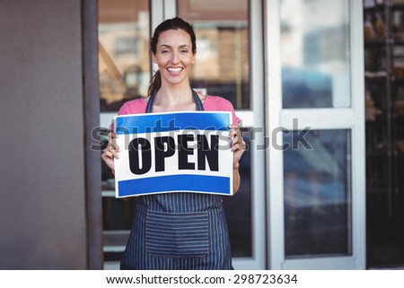 Pretty worker showing open sign at the bakery