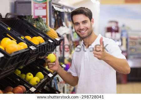 Portrait of a smiling handsome man buying a fruit with thumb up at supermarket