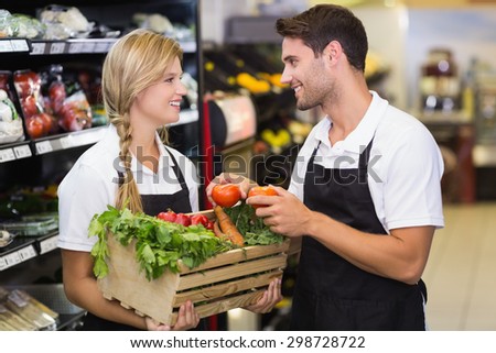 Smiling colleagues holding a box with fresh vegetables at supermarket