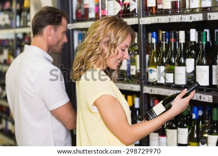 Smiling pretty woman looking at wine bottle in supermarket