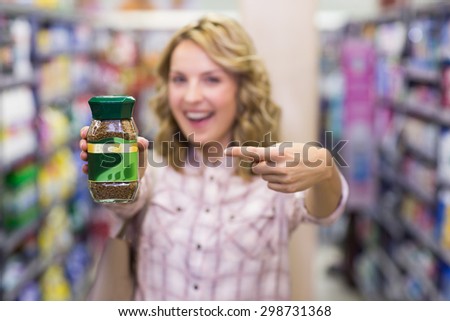 Happy smiling blonde woman showing a product in supermarket