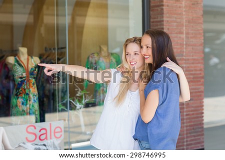 Smiling girl friends with arms around pointing away