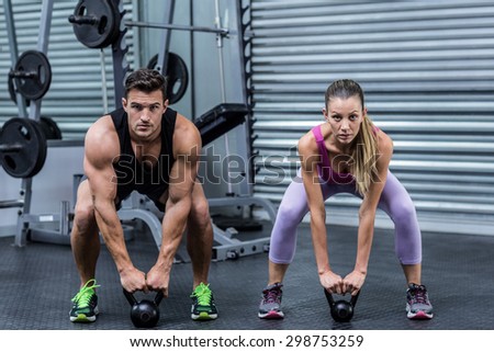 Portrait of a muscular couple lifting kettlebells at the health club