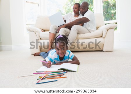 Pretty couple using laptop on couch and their daughter drawing in living room