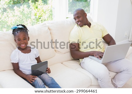 Happy smiling father using laptop and her daughter using tablet on couch in living room