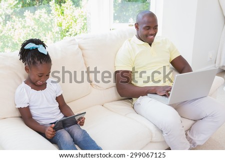 Happy smiling father using laptop and her daughter using tablet on couch in living room