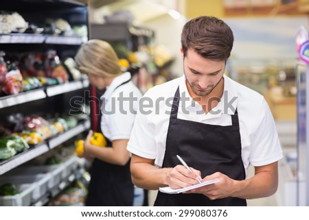 Serious staff man writing on notepad at supermarket