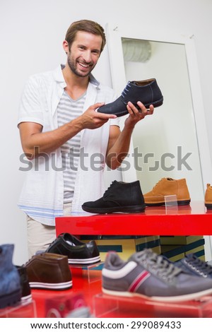 Young happy smiling man looking at the camera while holding a shoe in the shoe store