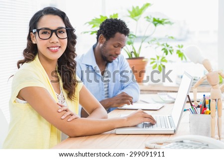 Pretty young businesswoman smiling at the camera with a businessman behind her in the office.