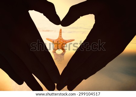 Woman making heart shape with hands against starfish on the sand