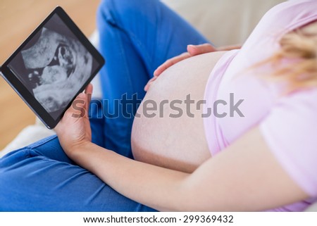 Pregnant woman looking at ultrasound scans and touching her belly in the living room