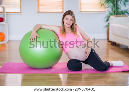 Pregnant woman looking at camera with exercise ball in the living room