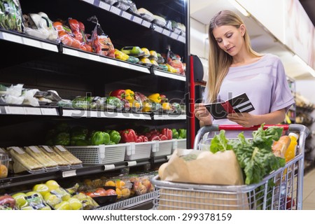 Smiling woman reading on his notepad in aisle at supermarket