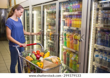 Pretty woman looking at camera and taking product on Pretty woman taking botlte of water in freezer at supermarket