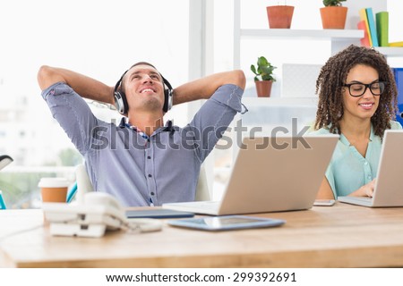 Relaxed businessman listening to music while his colleague working on laptop