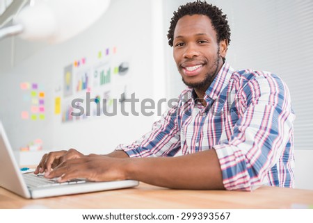 Young businessman types on the laptop and looks at the camera in the office