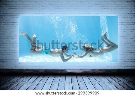 Cute couple holding hands underwater in the swimming pool against room with screen