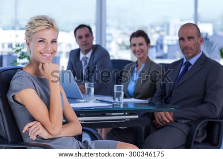 Businesswoman smiling at camera with colleagues behind in the office
