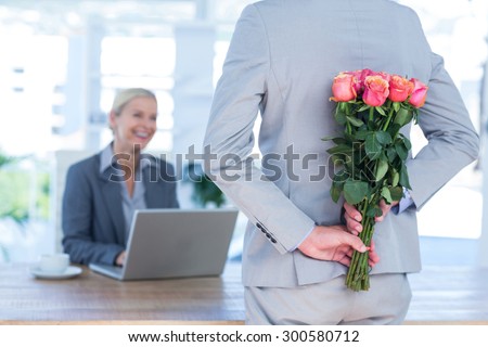 Businessman hiding flowers behind back for colleague in an office