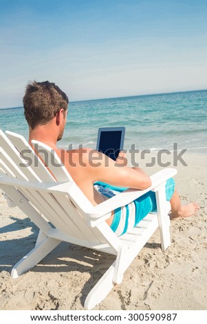 Man using digital tablet on deck chair at the beach on a sunny day