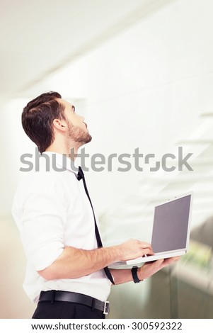 Sophisticated businessman standing using a laptop against stylish modern home interior with staircase