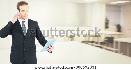 Serious businessman on the phone holding tablet against empty class room