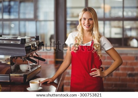 Portrait of a pretty barista with hands on hips at the coffee shop