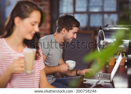 Smiling young man sitting at bar and using laptop at coffee shop