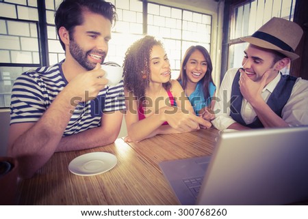 Laughing friends drinking coffee and looking at laptop at coffee shop