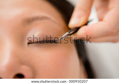 Close up view of woman placing fake eyelash on a patient at the spa health