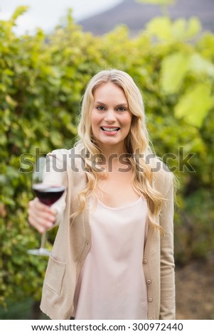 Young happy woman holding a glass of wine and looking at camera in the grape fields