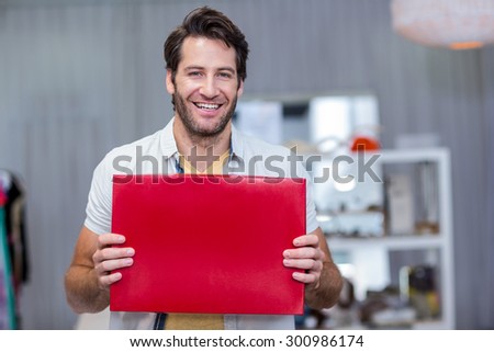 Portrait of smiling man holding up red blank sign in clothing store