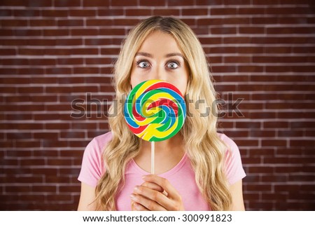 A beautiful woman holding a giant lollipop against a red brick wall