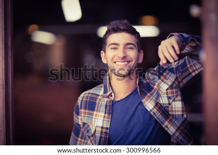 Portrait of smiling casual waiter leaning against door at coffee shop