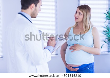 Pregnant patient talking to doctor which is taking notes in medical office
