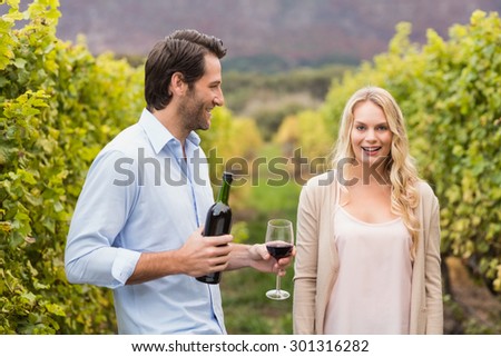 Young happy man offering wine to a young woman in the grape fields
