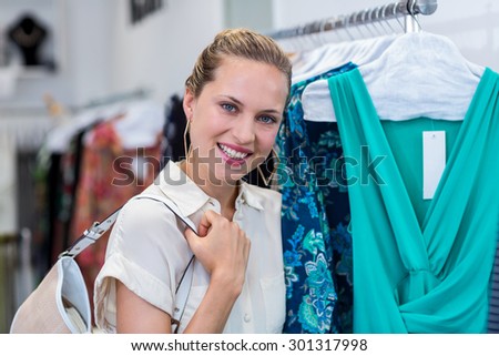 Portrait of smiling woman standing next to clothes rail in clothing store