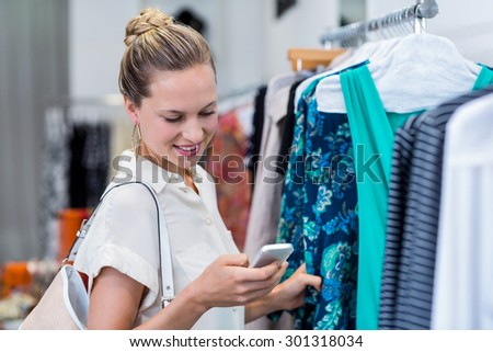 Smiling woman using smartphone while browsing clothes in clothing store