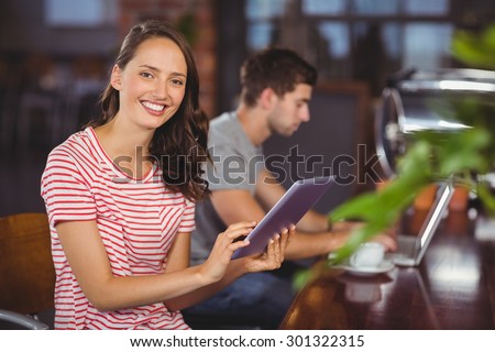 Portrait of smiling young woman using tablet computer in front of her friend at coffee shop