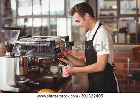 Smiling barista steaming milk at coffee machine at coffee shop