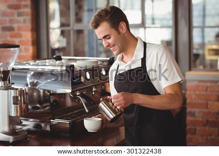 Smiling barista pouring milk into cup at coffee shop